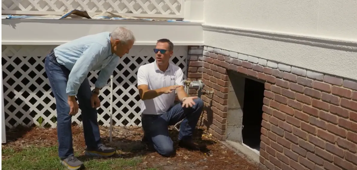 A Metro Foundation Solutions specialist explains a crawl space issue to a homeowner beside the foundation wall
